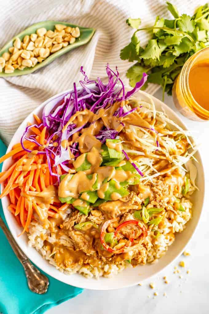 A rice bowl with shredded cabbage, carrots and peanut chicken all drizzled with a peanut dressing and sprinkled with sliced green onions.