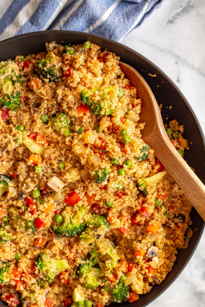 Quinoa fried rice in a large pan with a wooden spoon scooping out
