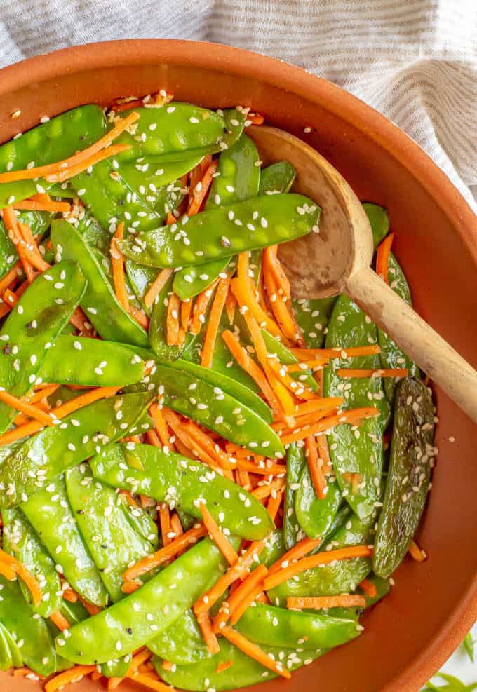Sautéed snow peas and carrots in a pan with sesame seeds on top