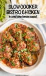 A serving spoon resting in a large round white serving dish with chicken thighs in a red wine and tomato sauce with fresh herbs sprinkled over top and a bowl of mashed potatoes in the background.