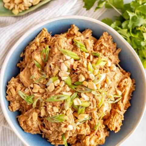Slow cooker peanut chicken served in a blue bowl with chopped peanuts and sliced green onions