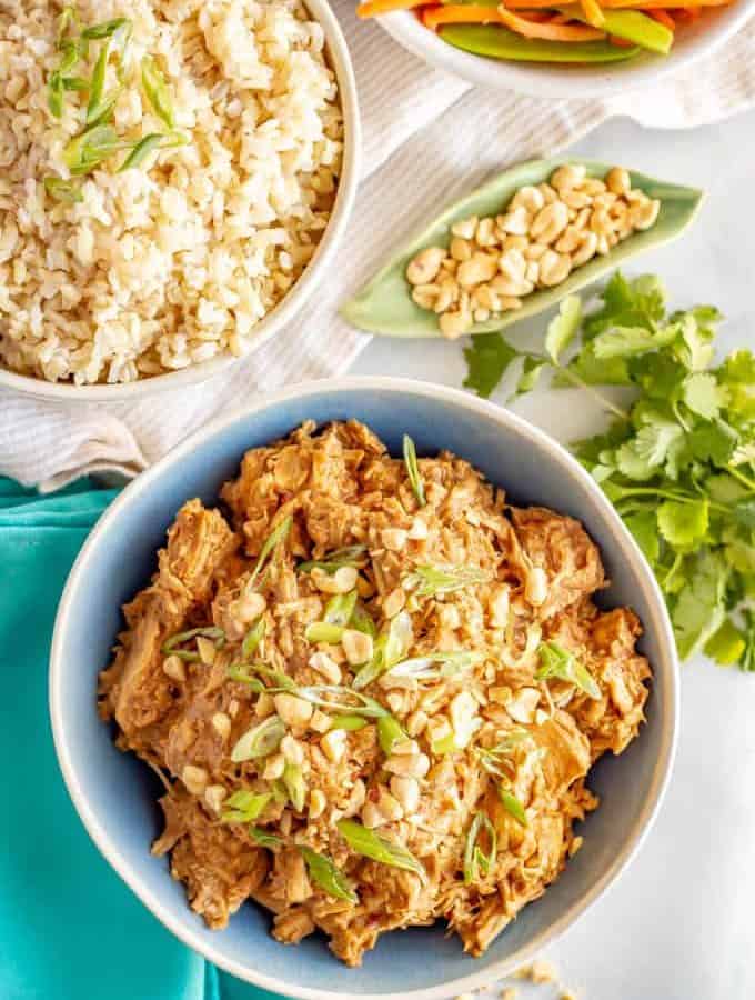Slow cooker peanut chicken served family style with bowls of brown rice and veggies nearby