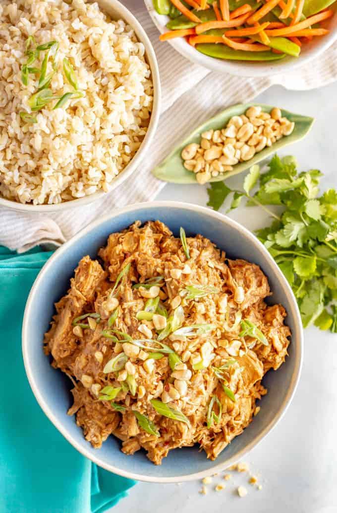 Slow cooker peanut chicken served family style with bowls of brown rice and veggies nearby