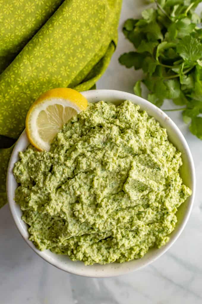 A white bowl with spicy edamame dip and a lemon wedge and cilantro alongside