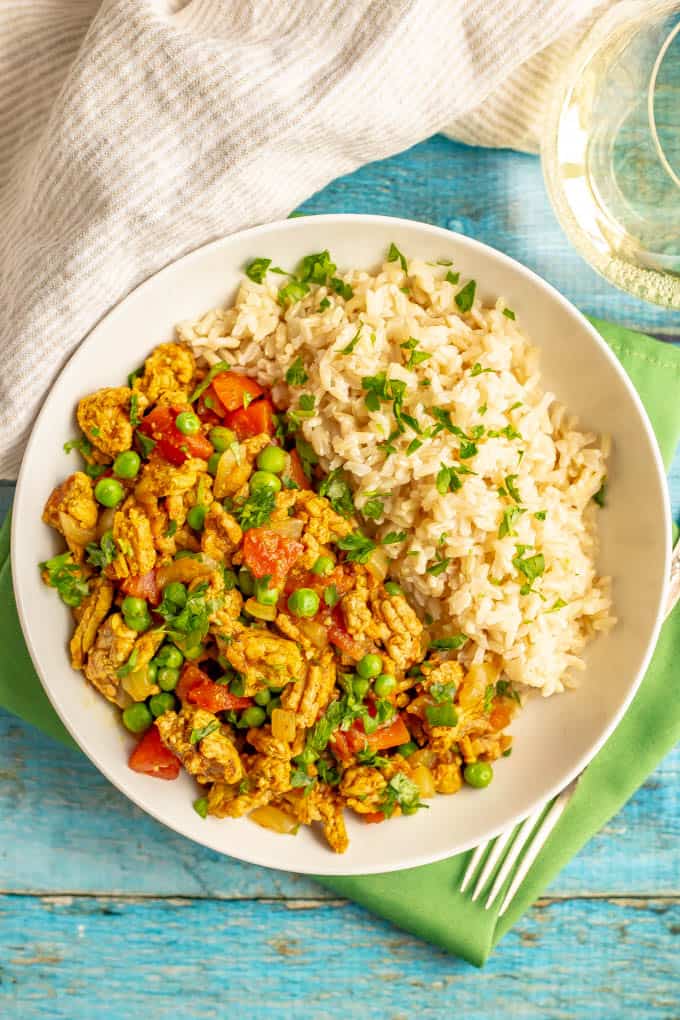 Curry ground turkey with peas and rice served in a white bowl with a glass of wine nearby
