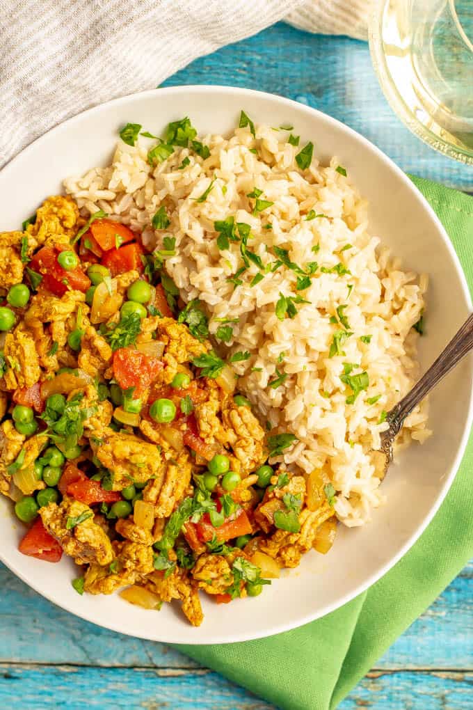 Curried ground turkey with rice and peas topped with cilantro and served in a bowl with a fork