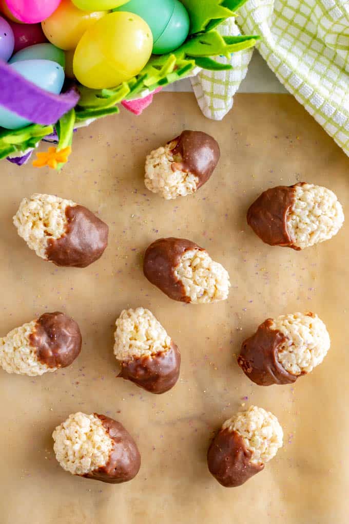 A collection of chocolate dipped Easter Rice Krispie treats on wax paper with an Easter basket