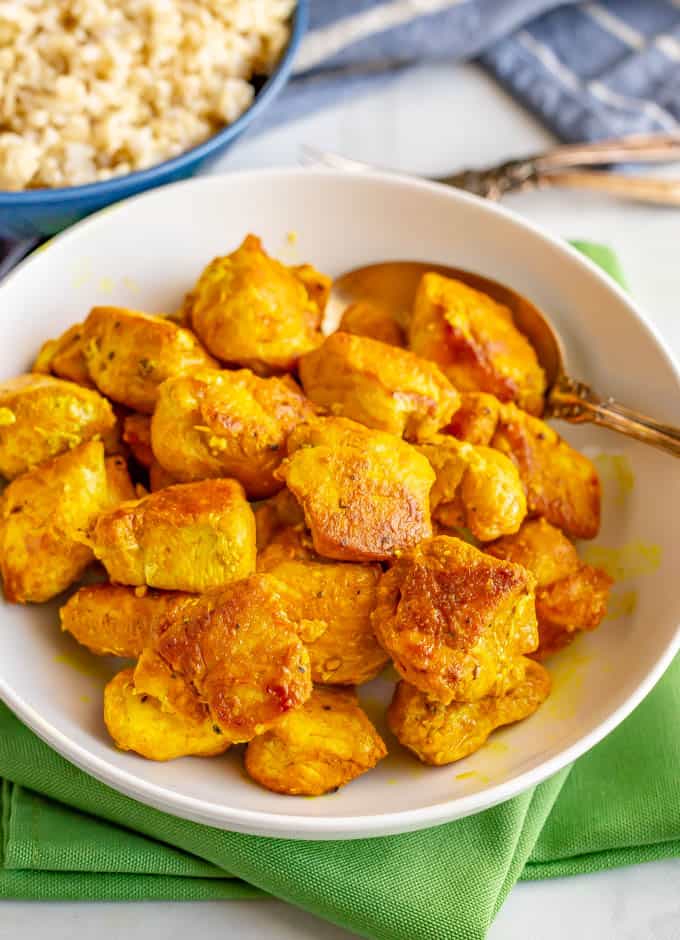 A white serving bowl full of pieces of turmeric spiced chicken pieces