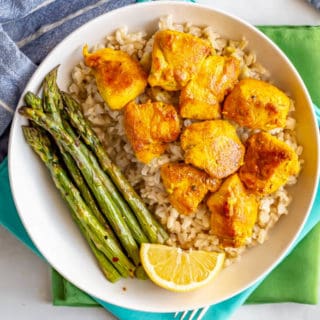 Turmeric chicken chunks served in a large white bowl over rice with asparagus on the side