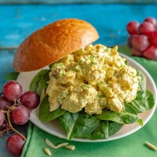 Curry chicken salad served as a sandwich on a bun with red grapes alongside