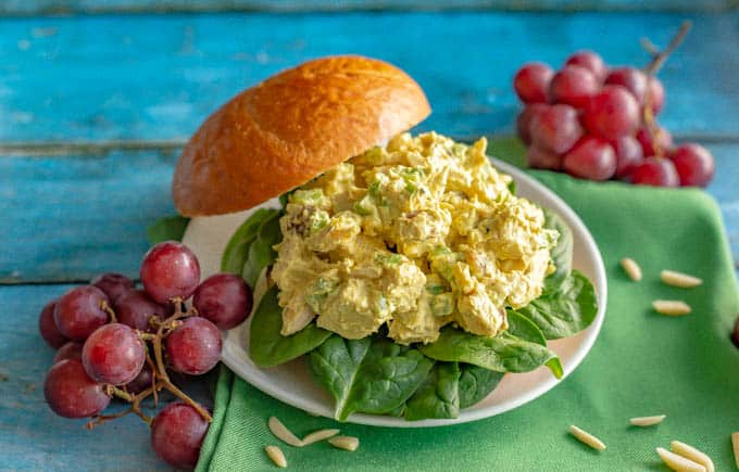 Curry chicken salad served as a sandwich on a bun with red grapes alongside