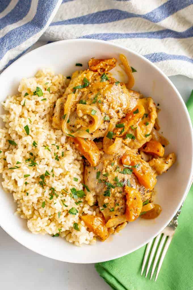 An apricot chicken mixture with onions served alongside steamed brown rice in a white bowl.