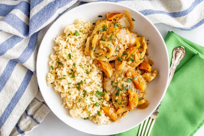 A white bowl with steamed rice and chicken with apricots and onions