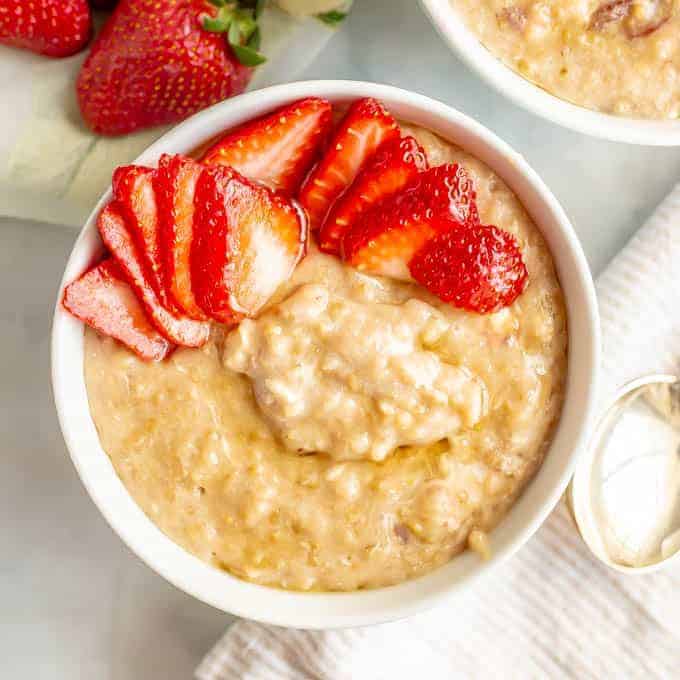 Close up of slow cooker strawberries and cream oatmeal served in a white bowl with fresh strawberries