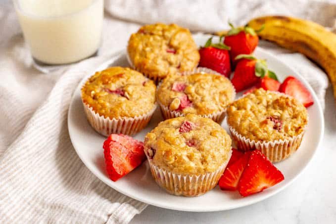 Whole grain strawberry banana muffins served on a white plate with sliced strawberries