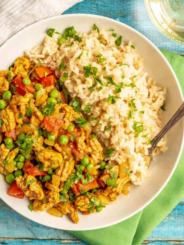 A large white bowl with brown rice and a curried ground turkey mixture with peas with chopped cilantro sprinkled over everything