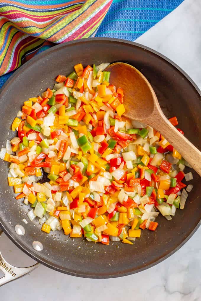 Mixed color bell peppers and onions sautéed in pan