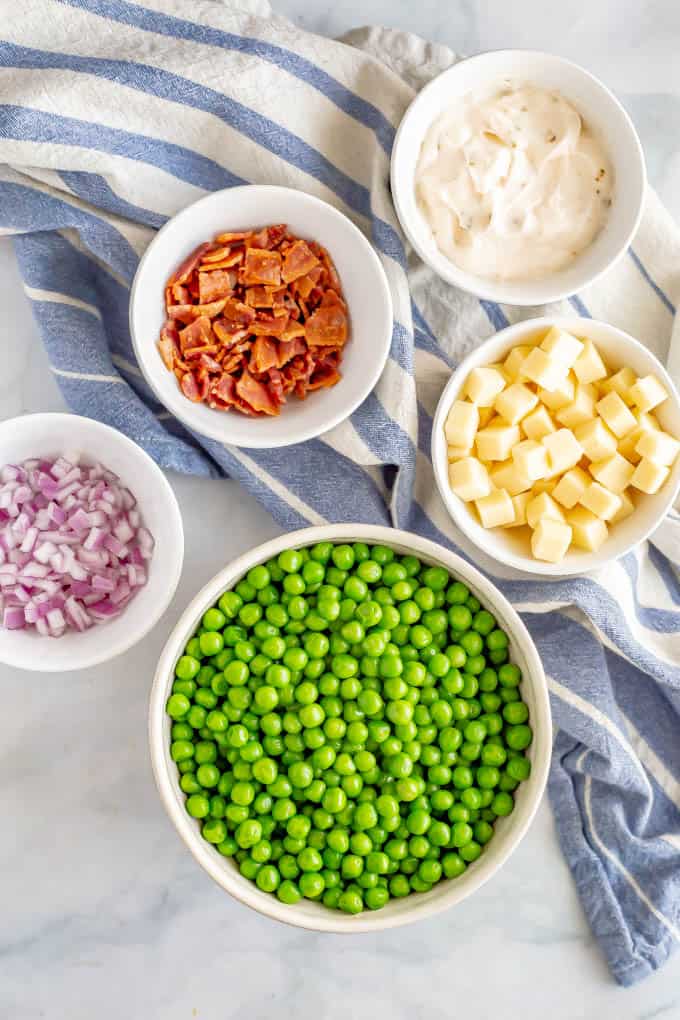 Ingredients for pea salad in separate white bowls with a blue napkin underneath