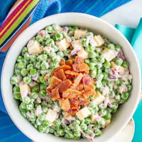 Creamy pea salad with cheddar cheese and bacon in a large white serving bowl