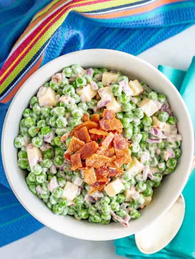 Creamy pea salad with cheddar cheese and bacon in a large white serving bowl
