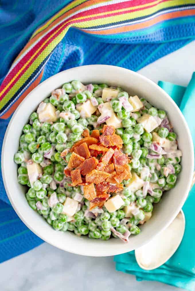 Creamy pea salad with cheddar cheese and bacon in a large white serving bowl