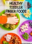 A colorful mix of plates with several different finger foods for toddlers on each one and a hand reaching in for some strawberries on one of the plates.