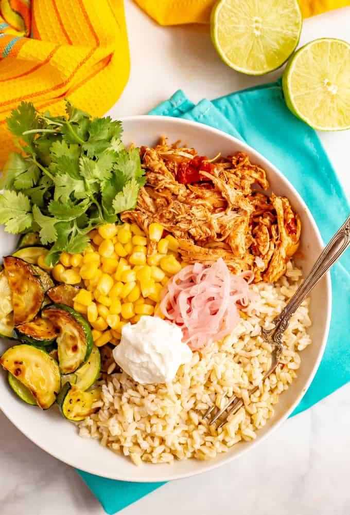 Healthy grain bowl with brown rice, salsa chicken, corn and zucchini, plus toppings in a large white bowl