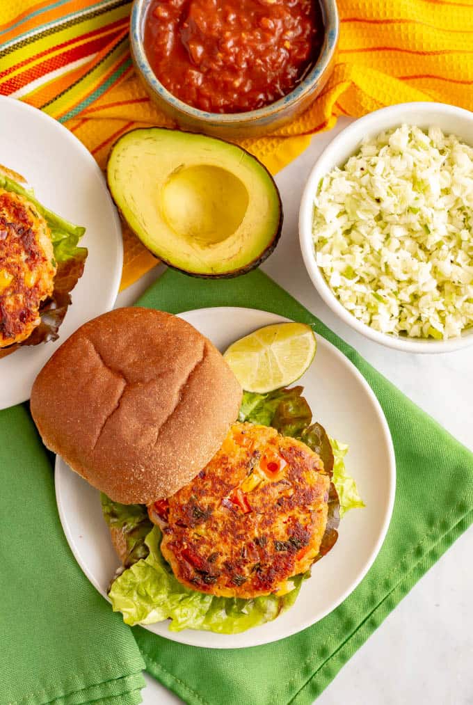Southwest salmon patties served on white plates with sides of coleslaw, salsa and avocado
