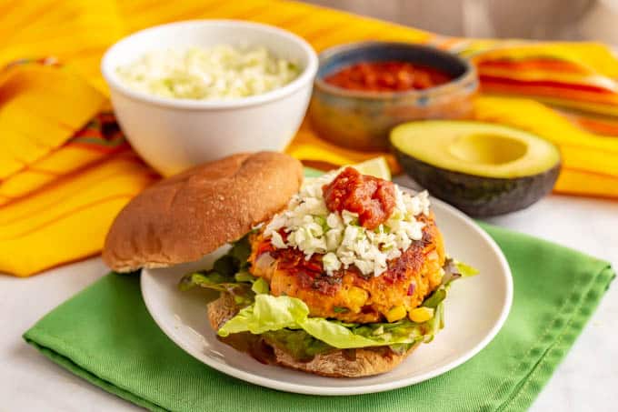 A southwest-style salmon burger served on a bun with lettuce and coleslaw and salsa on top