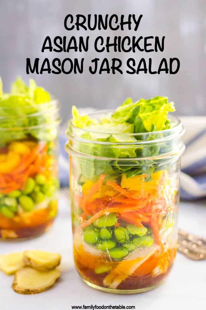 A layered Asian chicken salad in a glass mason jar with edamame, carrots and lettuce and a soy ginger dressing at the bottom