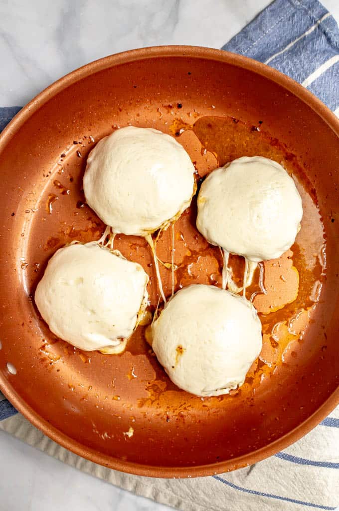 Four Italian chicken burgers covered in melted mozzarella cheese in a large skillet