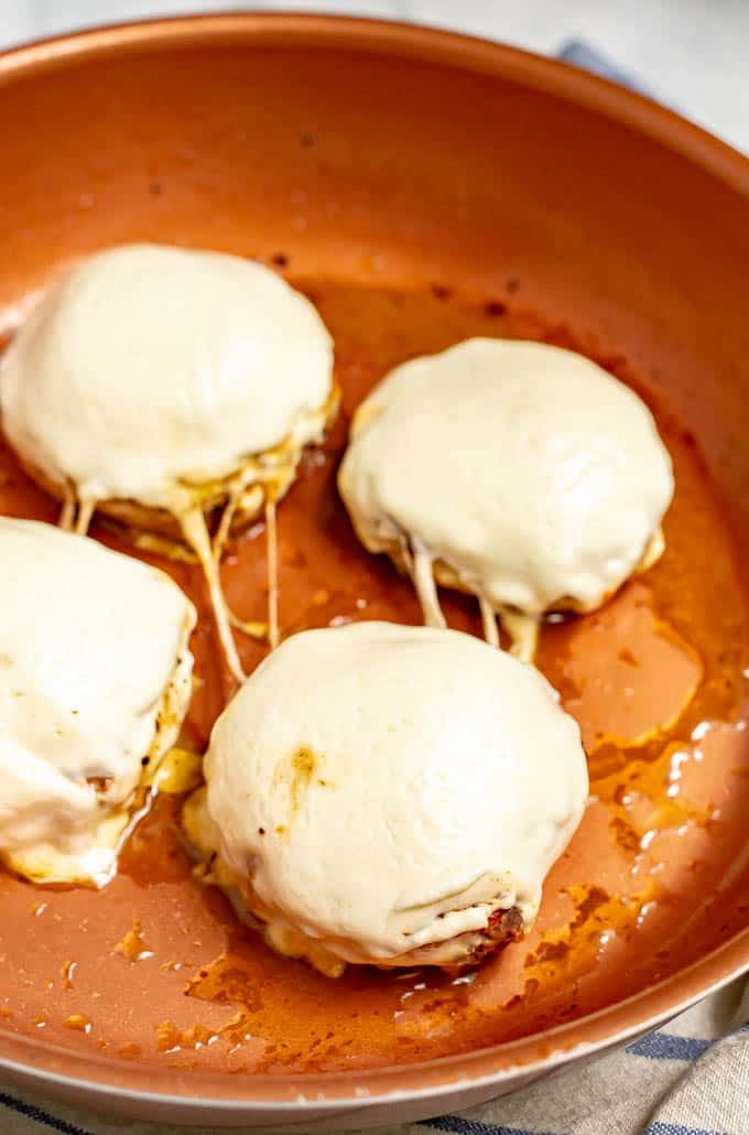 Italian chicken burgers with melted mozzarella cheese after cooking in a skillet