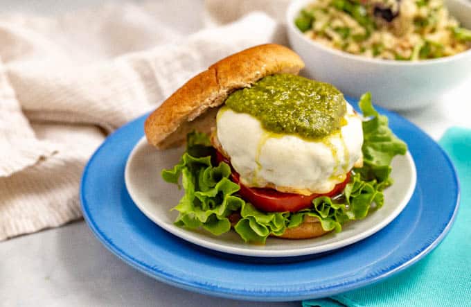 A mozzarella covered chicken burger with pesto on top served on a bun with fixings