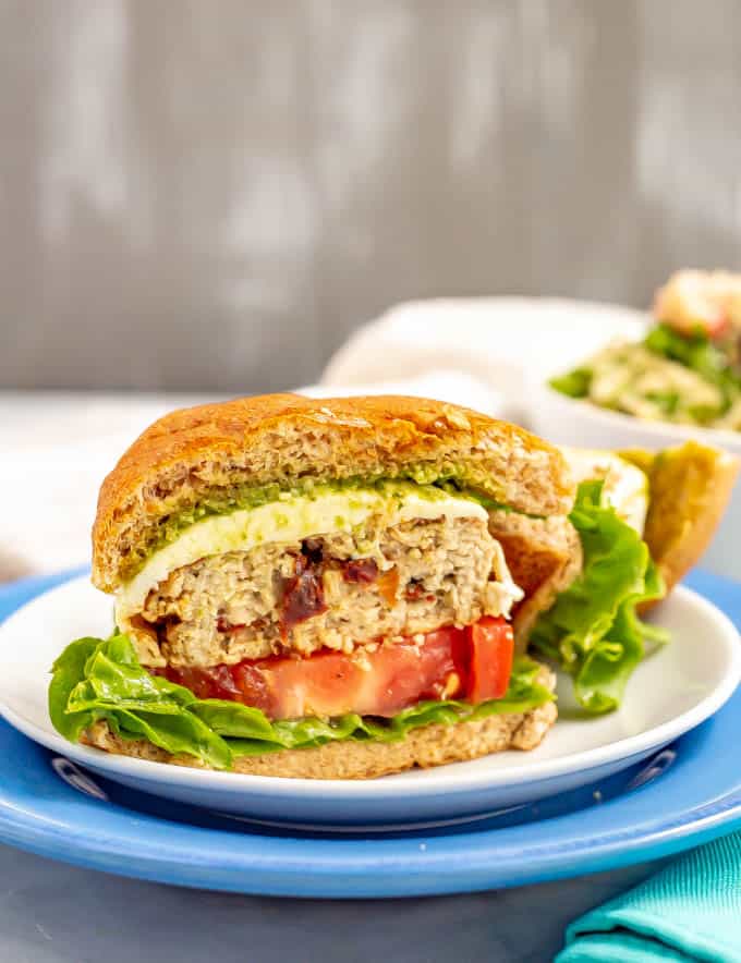 An Italian chicken burger sliced in half and served with lettuce, tomato, mozzarella cheese and pesto on a bun