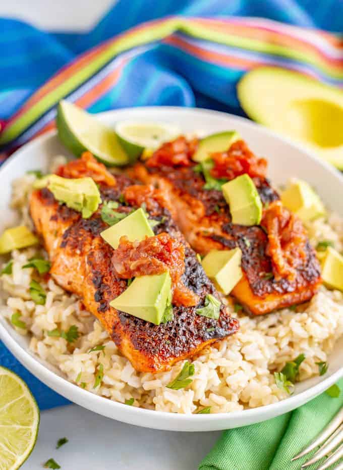 A bowl of rice topped with two filets of southwest baked salmon topped with salsa and diced avocado and chopped fresh cilantro.