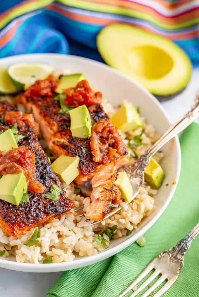 Close up of fork with a bite of roasted salmon topped with salsa and avocado