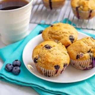 Whole wheat muffins with blueberries on a white plate with coffee and extra blueberries nearby