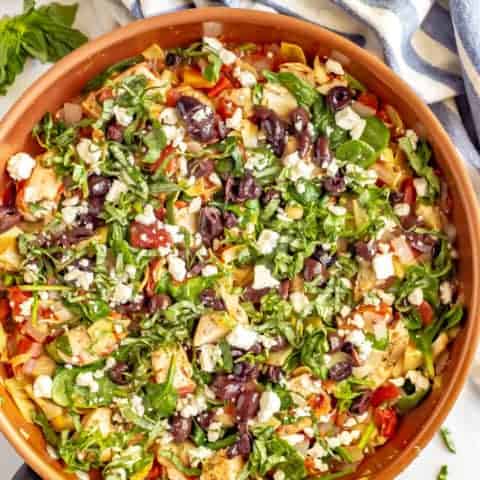 Full copper skillet of chicken and vegetables with basil on top and nearby and a lemon beside the pan