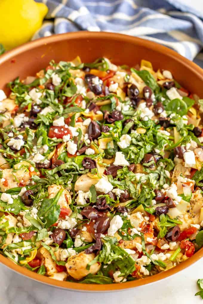 Copper skillet with cooked Mediterranean style chicken, artichokes, tomatoes and spinach with olives and feta on top