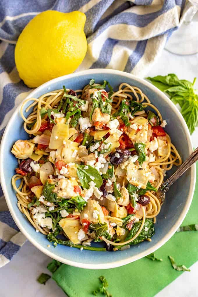 Chicken and veggies served over spaghetti noodles in a blue bowl with feta cheese on top