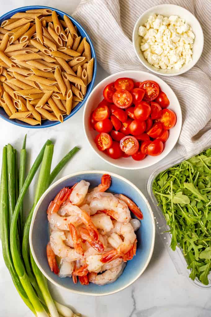 Ingredients laid out in separate bowls, including pasta, shrimp, tomatoes, feta cheese, scallions and arugula