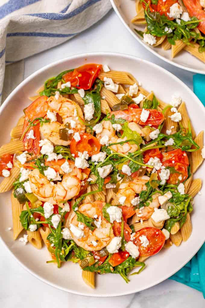 White bowl served up with shrimp penne pasta, arugula, tomatoes and feta cheese