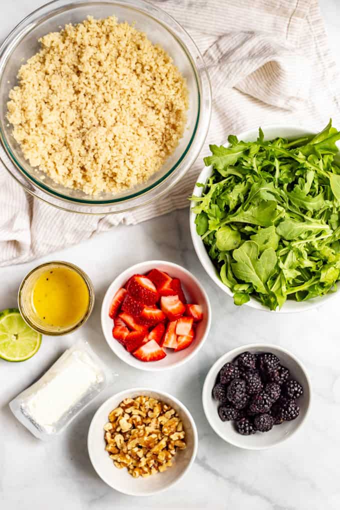 Ingredients for summer quinoa salad laid out in separate bowls on a marble countertop