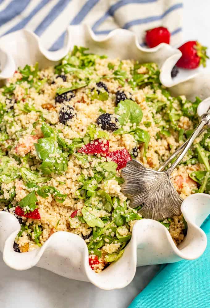 Summer quinoa salad with arugula, fresh berries and goat cheese being served from a large white bowl with a fluted edge