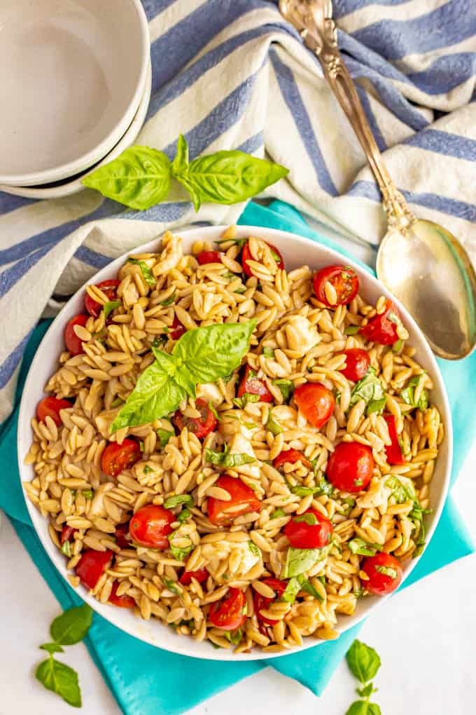 Pasta salad with tomatoes, mozzarella and fresh basil served in a white bowl