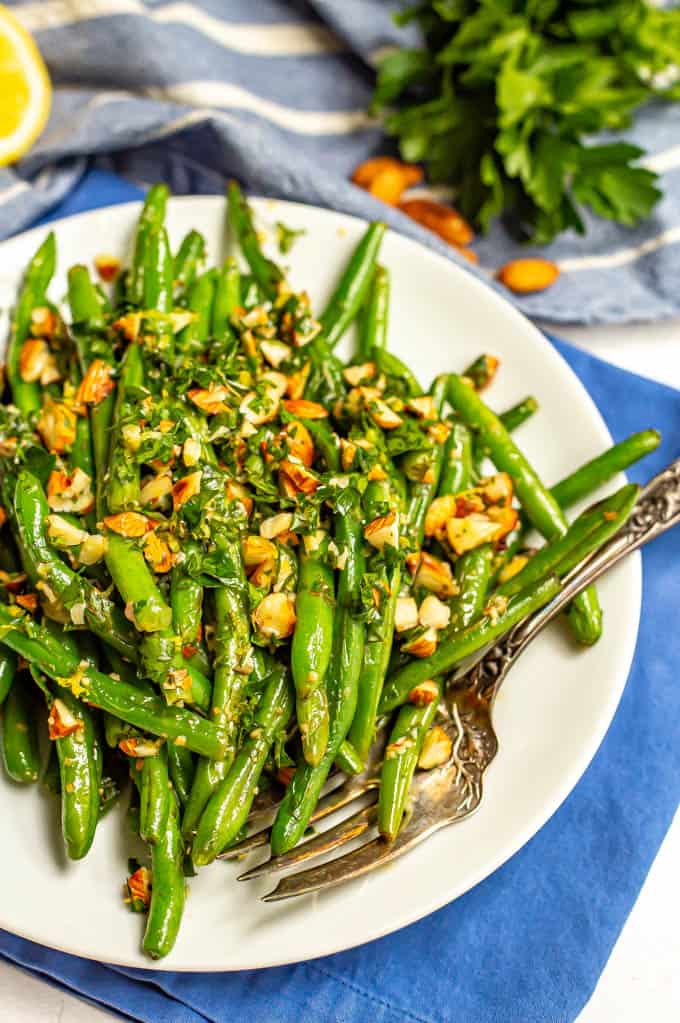 Green beans served on a plate with a sprinkling of almonds mixed with parsley and lemon juice with a fork on the plate