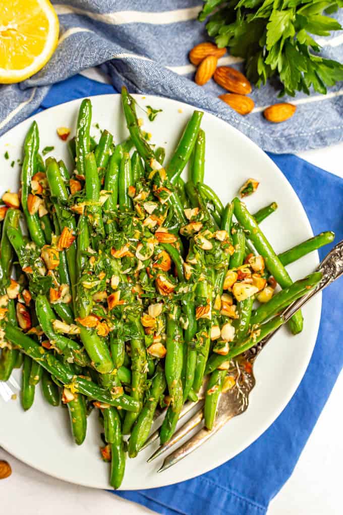 Green beans served on a plate with a sprinkling of almonds mixed with parsley and a fork along the side of the plate