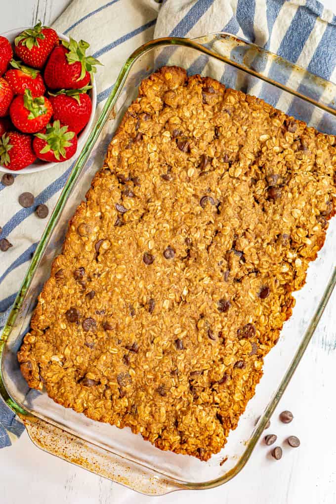 Granola bars in a glass pan after baking with a bowl of strawberries to the side