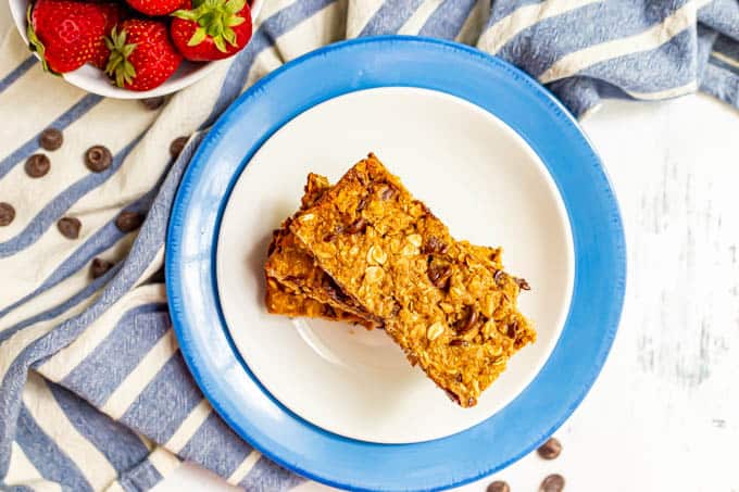 Overhead shot of granola bars stacked on top of each other on a white plate with a blue towel nearby