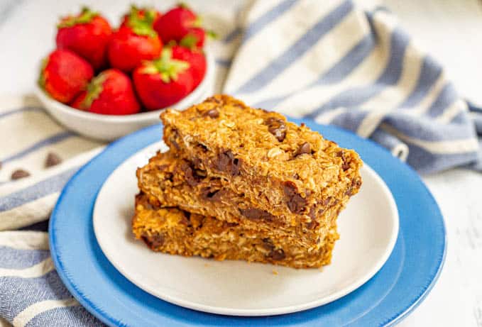 Chocolate chip granola bars stacked on a plate with a bowl of strawberries in the background